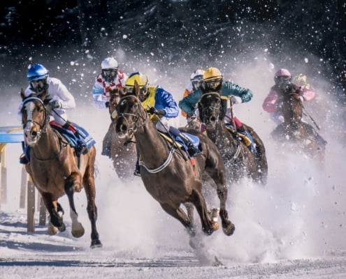 jockeys on racehorses racing through snow